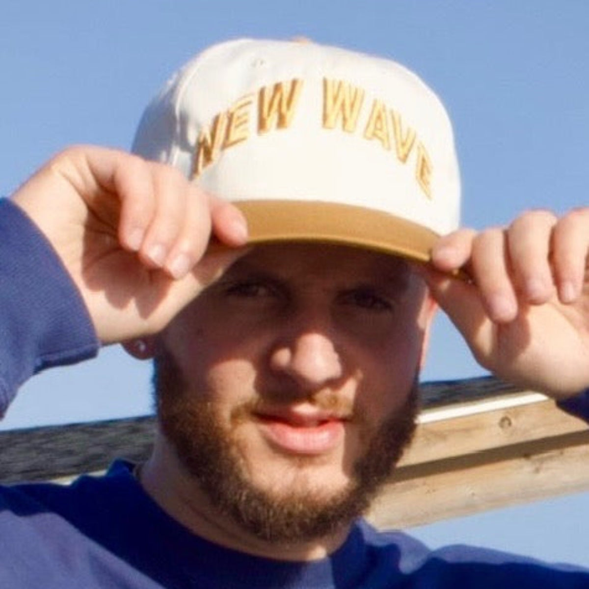 Man wearing a blue sweatshirt and a cap with 'New York' text, standing outdoors.