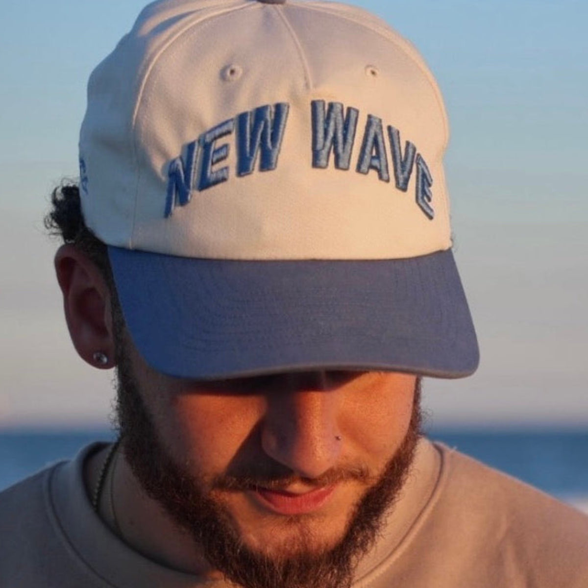 Man wearing a cap with 'NEW WAVE' text on a beach