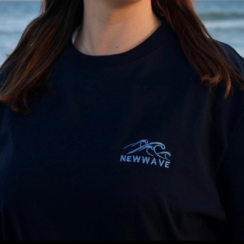 Person wearing a black shirt with 'NEWAVE' logo against a blurred natural background