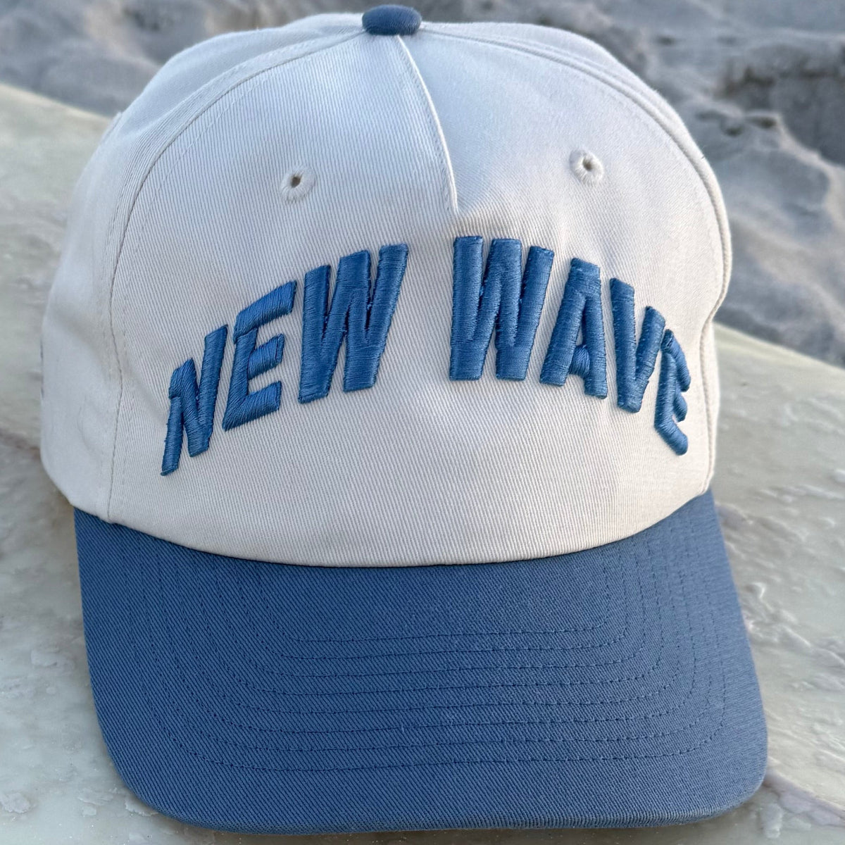 White and blue cap with 'NEW Wave' text on a sandy background