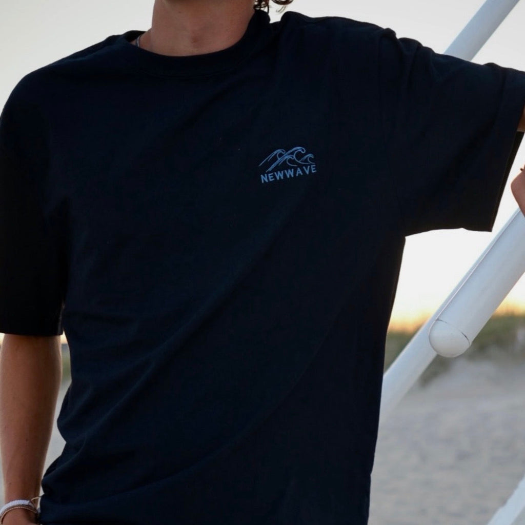 Person wearing a black t-shirt with a blue logo on a blurred outdoor background
