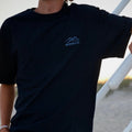 Person wearing a black t-shirt with a blue logo on a blurred outdoor background