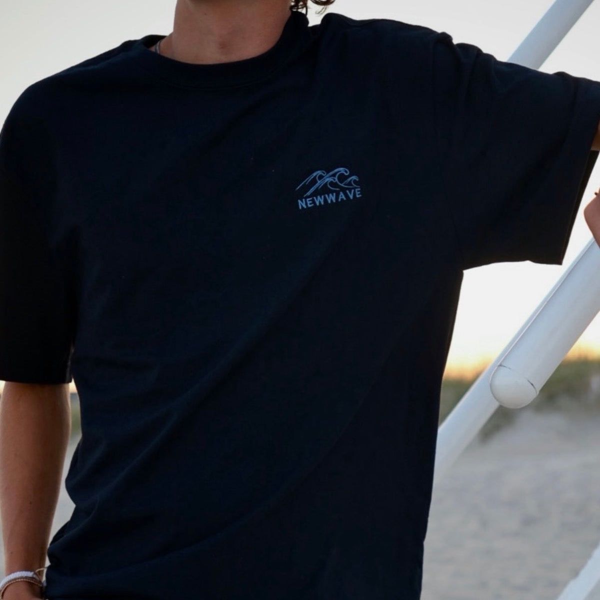 Person wearing a black t-shirt with a blue logo on a blurred outdoor background