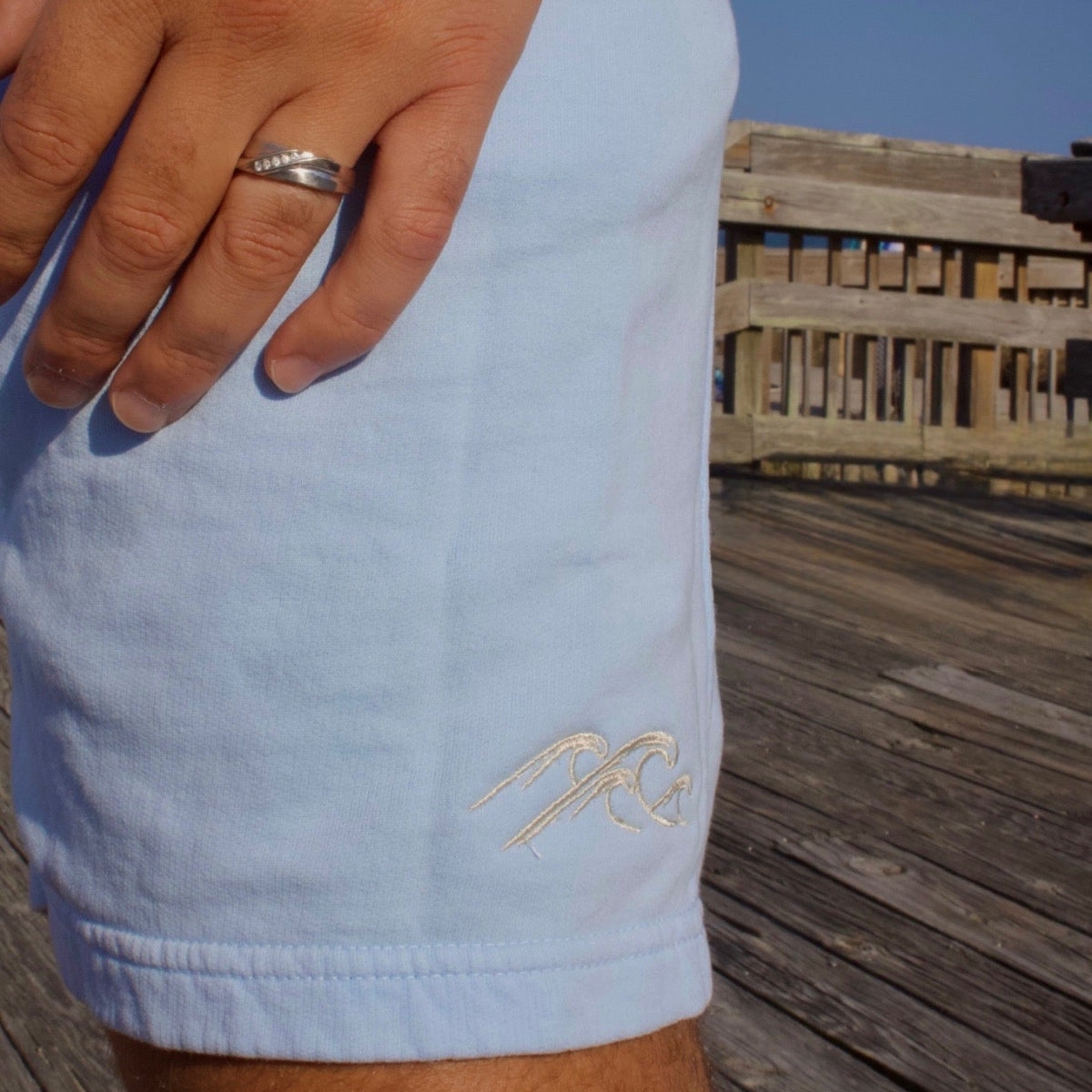 Light blue shorts with a logo on a wooden deck with a clear blue sky.
