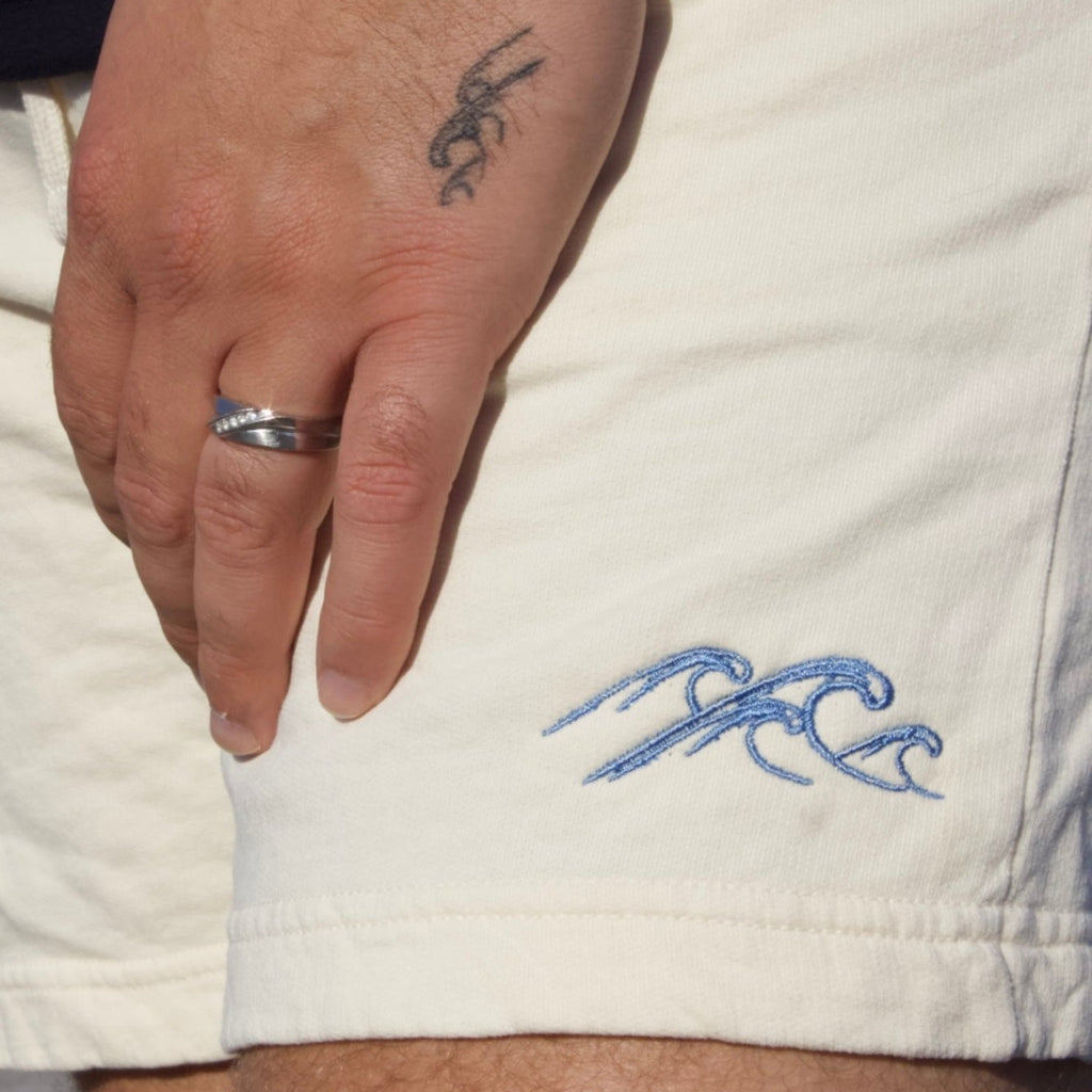 Hand with tattoo wearing a white garment with blue wave design