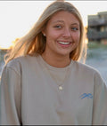 Woman wearing a beige sweatshirt with a logo, standing outdoors.