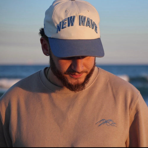 Man wearing a cap with 'NEW WAVE' text on a beach