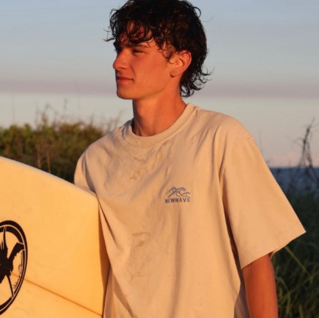 Man holding a surfboard with a sunset or sunrise in the background
